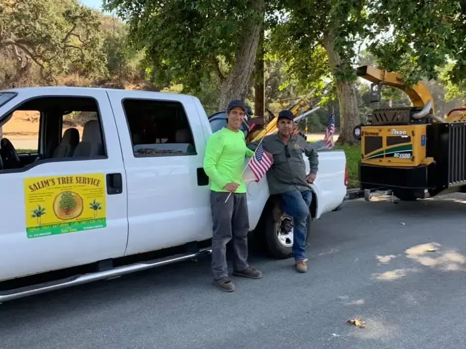 Salim and his son standing beside the branded Salim's Tree Service truck and chipper